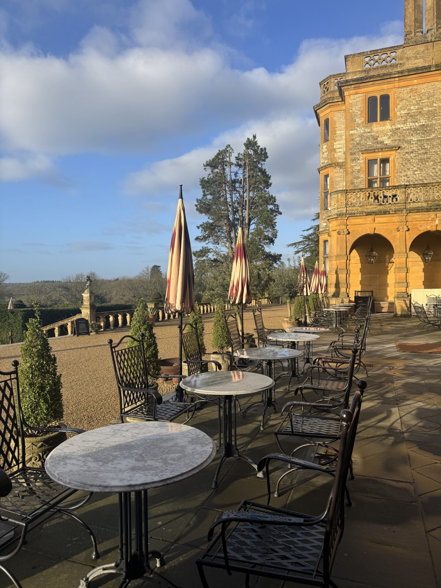Estelle Manor Oxfordshire Grounds with parasols and tables and chairs outside near a swimming pool